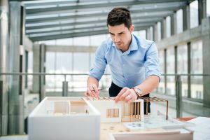 Young businessman or architect with model of a house standing in office, working.